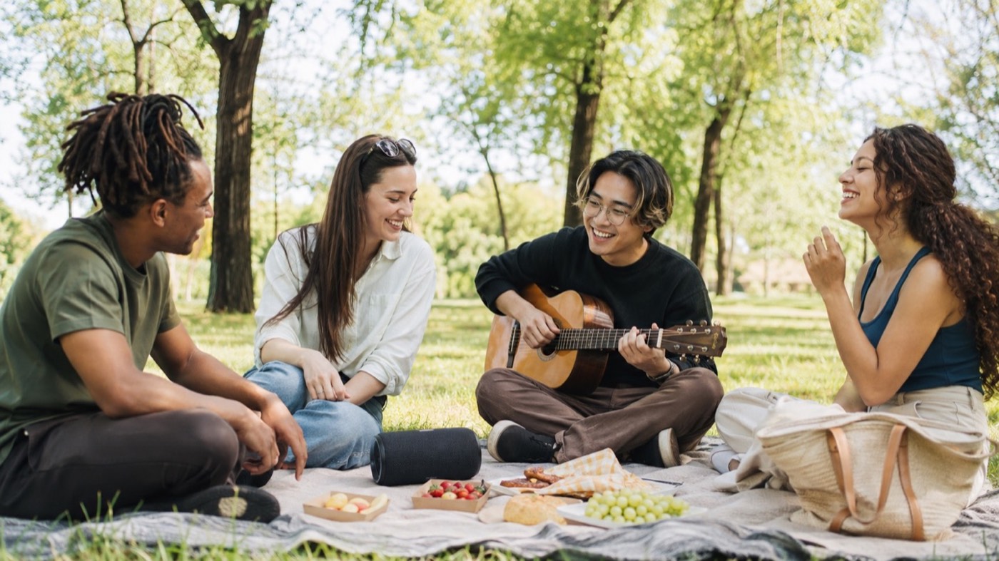 Friends sharing music from a portable Bluetooth speaker during a relaxed park picnic